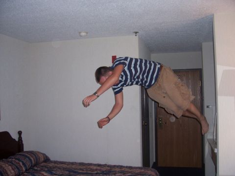 1990 Ford Probe - Man appears to be jumping or falling over a bed in a hotel room.