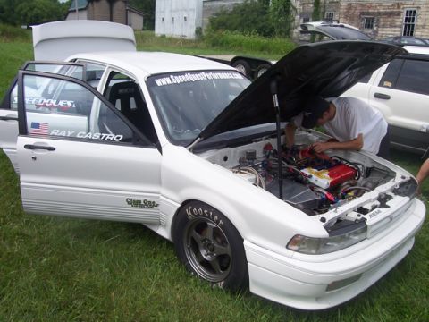 1990 Ford Probe - A white sedan with its hood and doors open, revealing its engine and interior, sits on grass with other vehicles nearby.