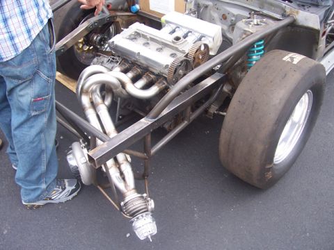 1990 Ford Probe - Custom drag car chassis with V6 engine, turbo, and exhaust headers. A person stands nearby.