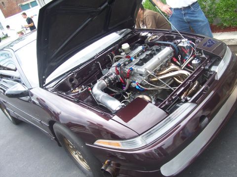 1990 Ford Probe - A customized engine bay is visible on a maroon car with its hood open, revealing extensive modifications.