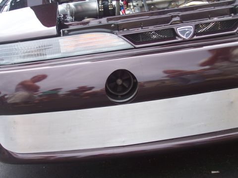 1990 Ford Probe - Close-up of a car's front bumper, showing a unique circular vent and a shield-shaped badge.