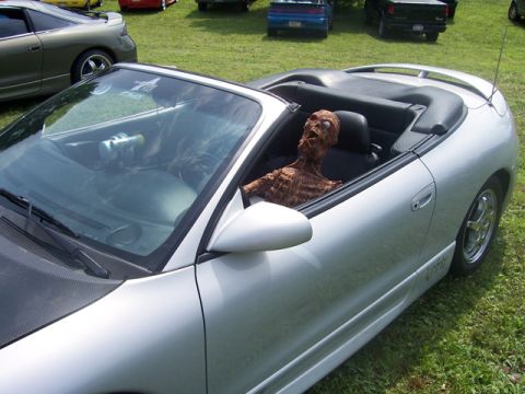 1990 Ford Probe - A zombie dummy is seated in a silver convertible parked on grass with other vehicles nearby.
