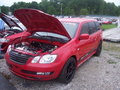 1990 Ford Probe - A red crossover SUV is parked with its hood open, revealing the engine bay. Another vehicle is parked beside it, also with its hood open.