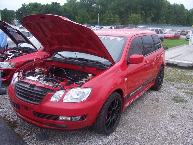 Red crossover SUV with hood open, showing engine. Another red car with hood open is next to it
