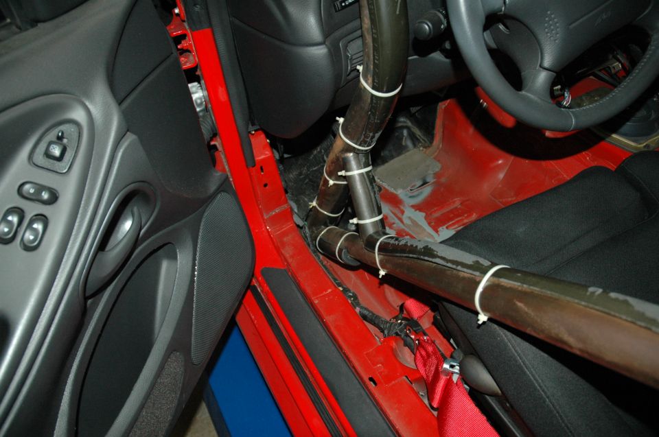 Interior shot of a car with a roll cage installed. Shows door panel, seat, steering wheel, and red floor