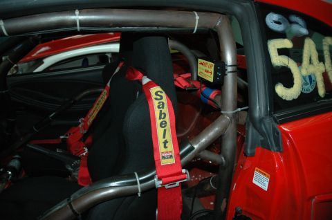 2000 Ford Mustang - The interior of a modified vehicle features a roll cage and racing seat with a Sabelt harness. Text on the window reads '02 540'.