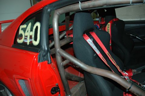 2000 Ford Mustang - The interior of a red vehicle is shown, a roll cage and racing seats with red harnesses.