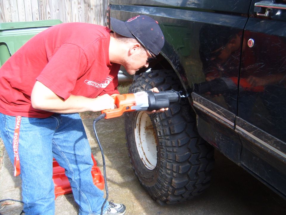 Guy using reciprocating saw to cut fender flare on a black SUV with large tires