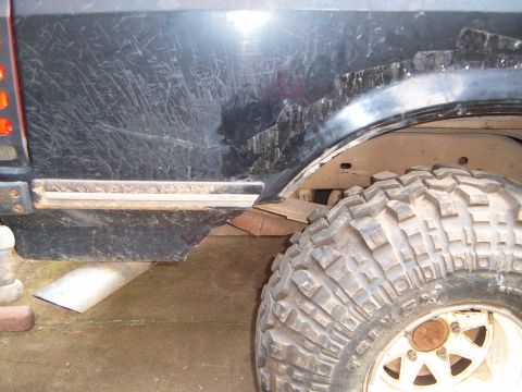 1988 Ford Bronco - Close-up of a heavily scratched rear fender and large off-road tire on a dark SUV.