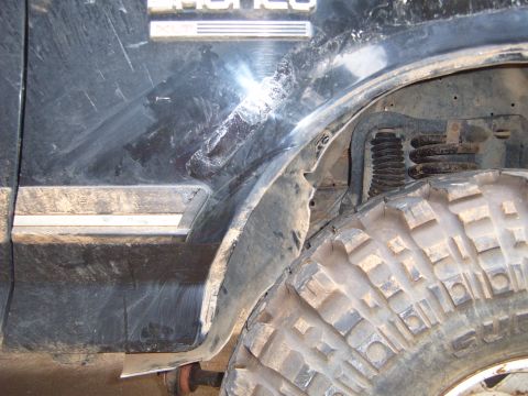 1988 Ford Bronco - Detail of the fender and wheel well of a black Ford Bronco, showing off-road tire and suspension components.
