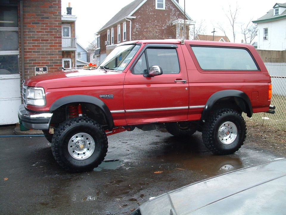 Red lifted full-size Ford Bronco with big tires and hardtop, side view