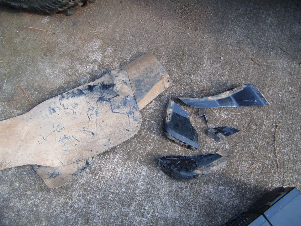 Broken black plastic fender trim pieces scattered on concrete