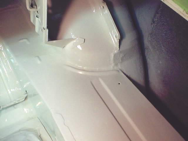 Close-up of a white painted floor pan inside a vehicle, showing structural details and seams