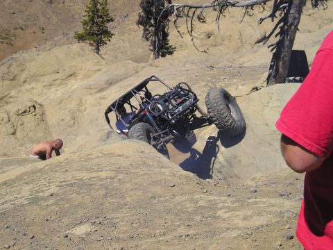 1989 Ford Bronco - A custom off-road buggy navigates a challenging rocky incline with a person assisting from the side.