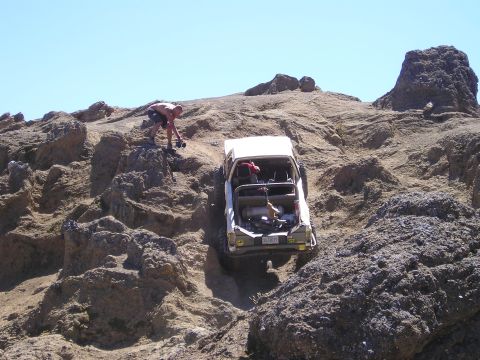 1989 Ford Bronco - A white SUV navigates a challenging rocky incline, with a person observing the ascent.