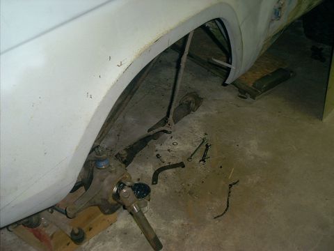 1990 Ford Bronco - The front suspension of a vehicle is shown with various tools scattered around it on the floor.