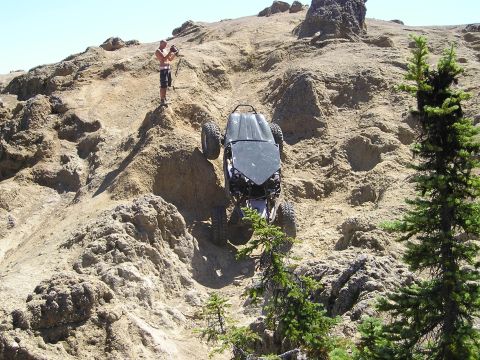 1989 Ford Bronco - A tube-chassis rock buggy climbs an extremely steep face of light tan volcanic rock, nose-up at a near-vertical angle on oversized mud tire…