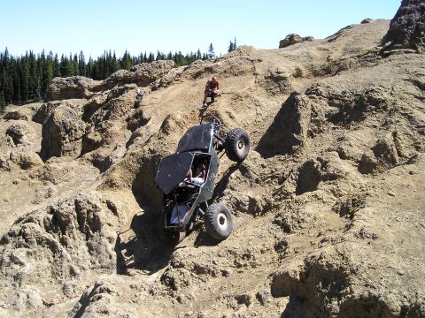 1989 Ford Bronco - A custom off-road vehicle navigates a challenging rocky incline under a clear blue sky.