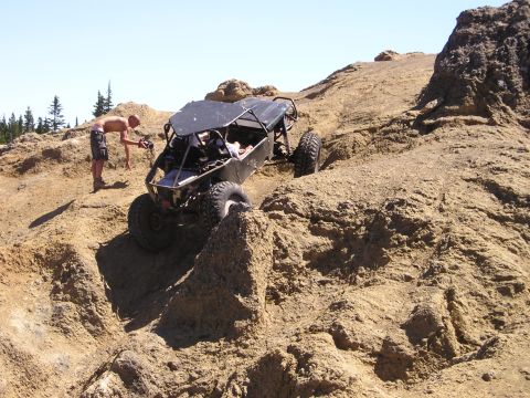 1989 Ford Bronco - Three-quarter front view of a black tube-frame rock buggy with a flat roof panel picking its way down a tan rock ledge, front tires droppin…