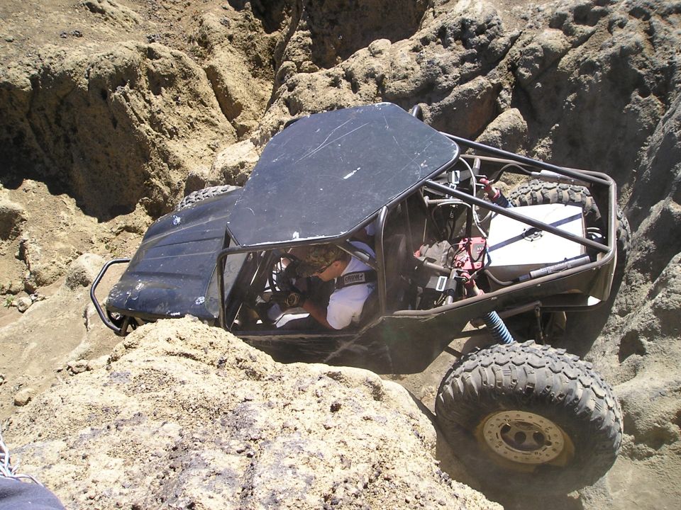 Overhead view of a black tube-chassis rock buggy with beadlock mud tires in a rock crevice