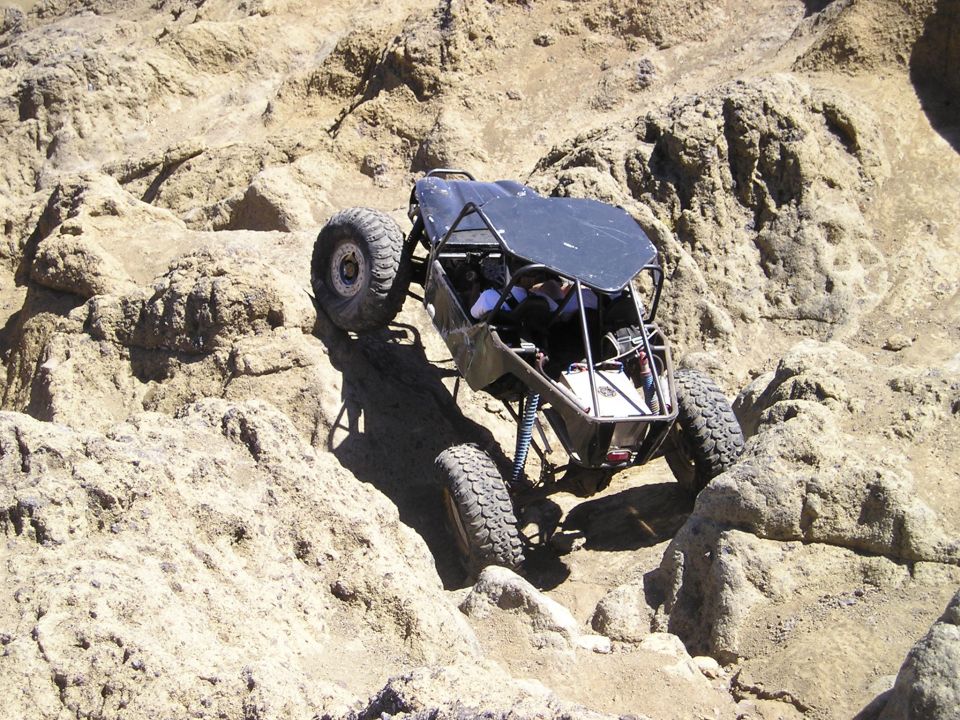 Tube-chassis rock buggy flexing over pale rock with front tire lifted on a ledge