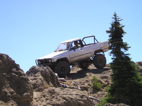 1989 Ford Bronco - A modified pickup truck navigates a challenging rocky terrain under a clear blue sky.