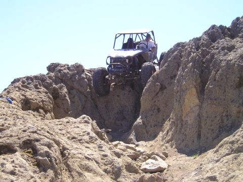 1989 Ford Bronco - An off-road buggy navigates a steep, rocky incline under a clear blue sky.