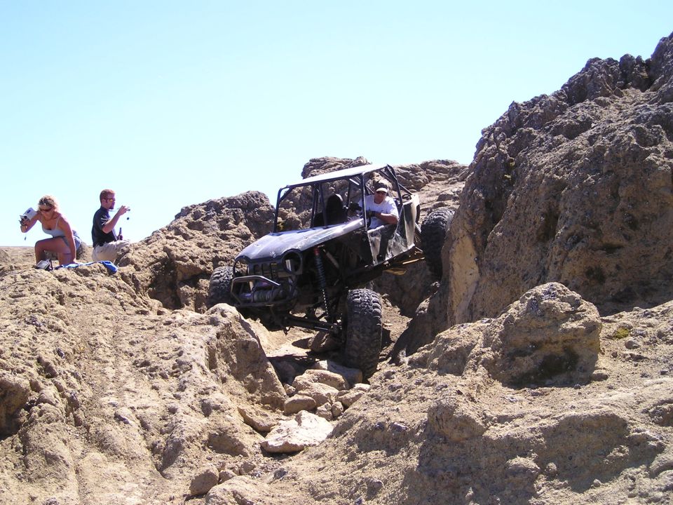 Off-road buggy with roll cage climbing over rocks, driver visible