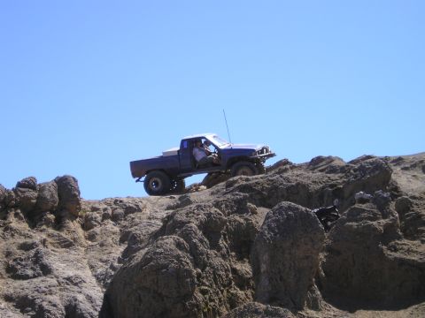 1989 Ford Bronco - Pickup truck navigates a steep, rocky incline under a clear blue sky.