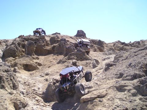 1989 Ford Bronco - Multiple off-road vehicles tackle a challenging rocky ascent on a sunny day.