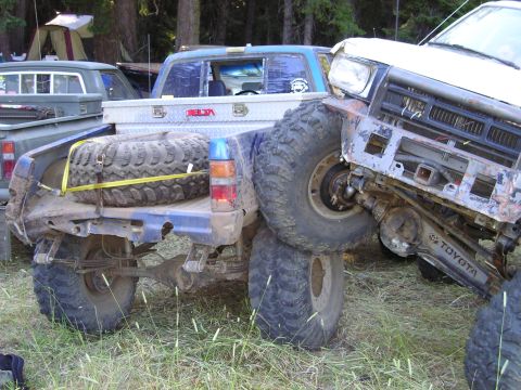 1989 Ford Bronco - Two modified trucks are entangled off-road, with one vehicle's front end lodged against the rear of another.