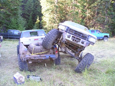1989 Ford Bronco - Two off-road trucks appear to be stuck in the mud, with one vehicle precariously balanced on top of the other.