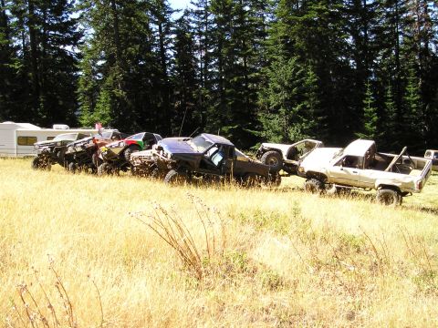 1989 Ford Bronco - A collection of off-road vehicles sits in a field, some appearing heavily modified.