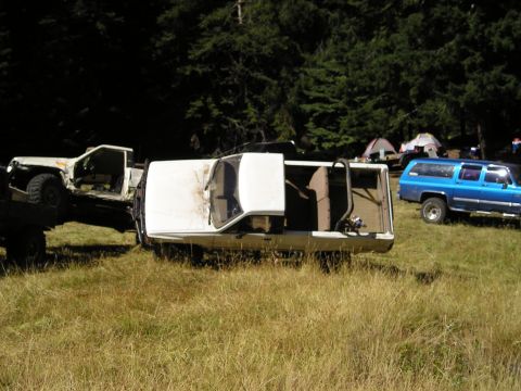 1989 Ford Bronco - Multiple vehicles are present in a grassy, wooded area with tents set up.