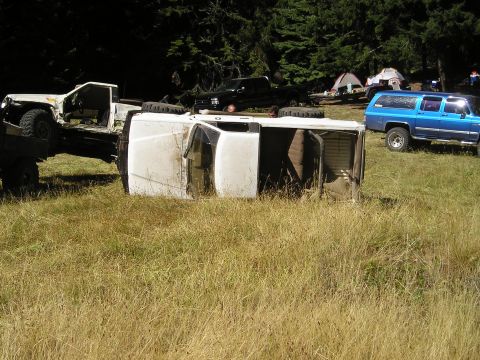 1989 Ford Bronco - Multiple vehicles are present in a grassy, wooded area, including an overturned white van.