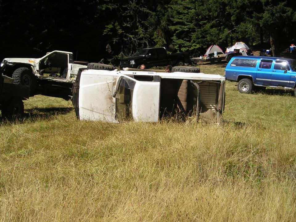 Overturned white van in tall grass with a blue SUV and a white truck nearby