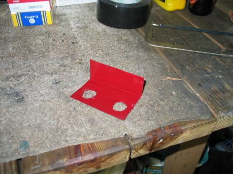 1995 Ford Bronco - A red metal bracket with two holes sits on a workbench, surrounded by tools and supplies.