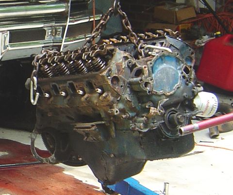 1986 Ford Bronco - A V8 engine, likely undergoing a swap, is hoisted by chains in a workshop setting.