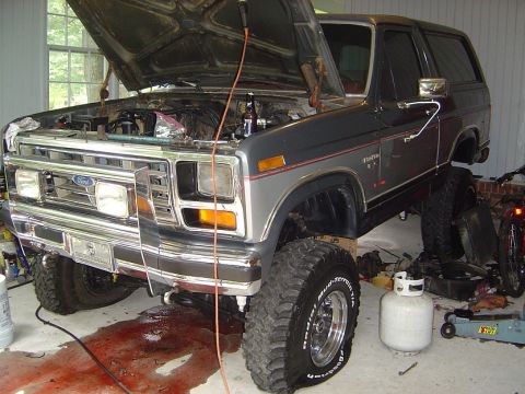 1986 Ford Bronco - Ford Bronco undergoing maintenance, hood open and engine exposed with fluid on the ground.