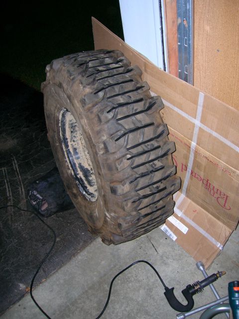 2003 Jeep TJ - A single, large off-road tire is shown leaning against a cardboard box, with tools visible on the ground.