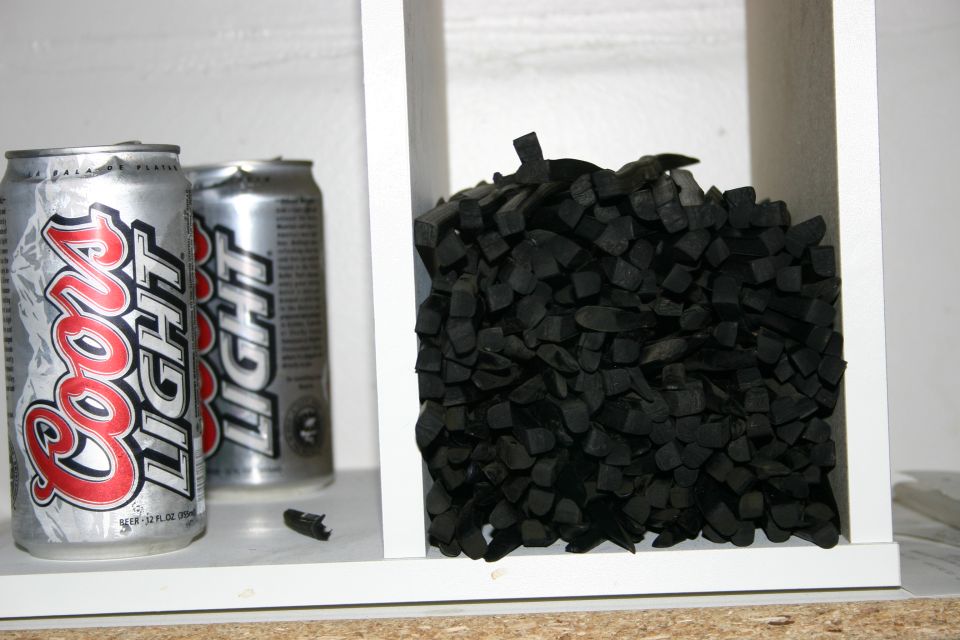 Two Coors Light beer cans next to a pile of black, chopped rubber pieces inside a white shelf