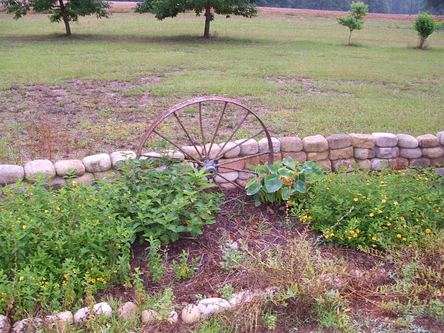 Old wagon wheel used as garden decor in front of a stone wall