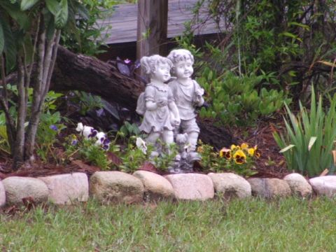 1966 Ford Ranchero - Two stone children statues are in a garden with flowers and grass.