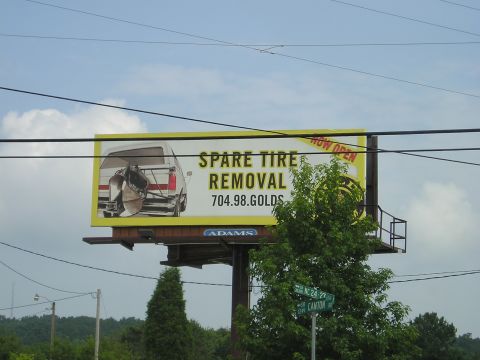 1996 Ford Bronco - A billboard advertises spare tire removal services with an image of a vehicle's rear.