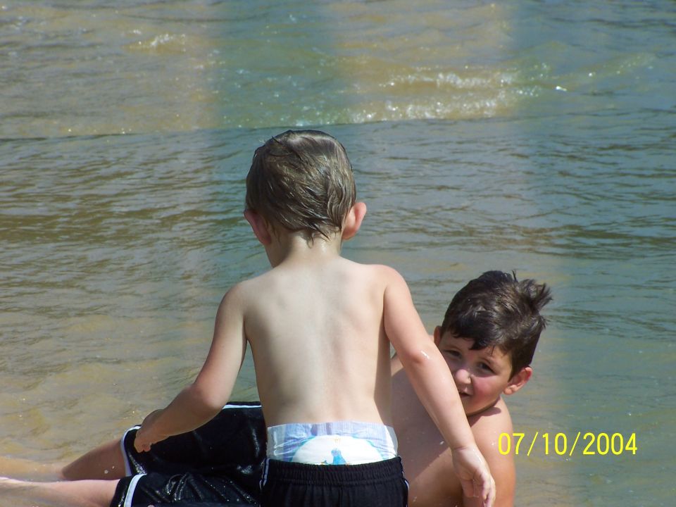 Two young boys are in the water, one facing away from the camera