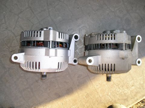 1993 Ford Bronco - Two alternators are displayed on a concrete floor, with one appearing newer than the other.