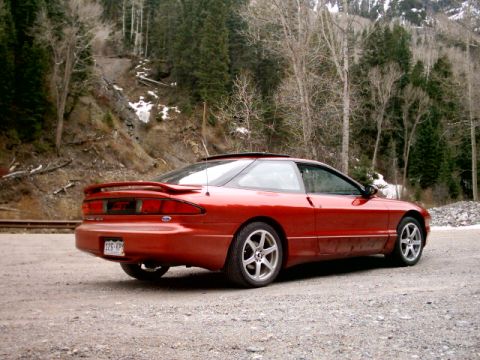 1996 Ford Probe - A red 1996 Ford Probe is parked on a gravel road, with a wooded mountain slope behind it.