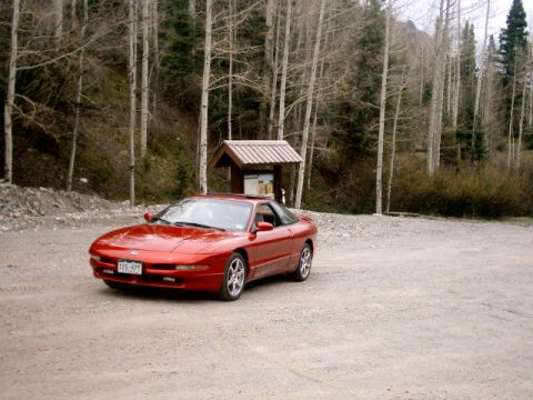1996 Ford Probe - A red 1996 Ford Probe coupe is parked in a gravel lot surrounded by trees. The vehicle is viewed from a three-quarter front angle.