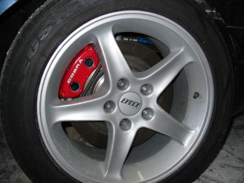 1987 Ford Thunderbird - A close-up shot focuses on a car's wheel, highlighting the silver rim and a red brake caliper with 'COBRA' branding.