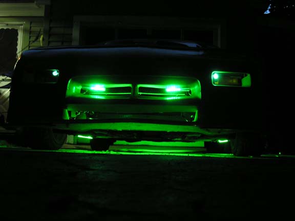 Front of a dark-colored car with green underglow lighting and green lights in the grille